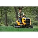 Man operating a yellow riding lawn mower in a park setting